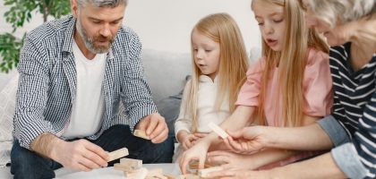 Four family members of different ages engage with toy blocks on a table indoors.