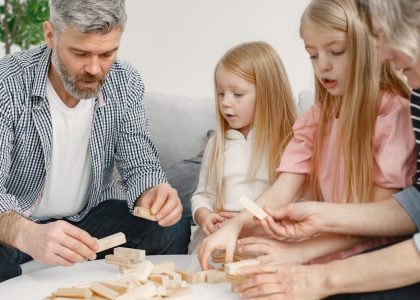 Four family members of different ages engage with toy blocks on a table indoors.