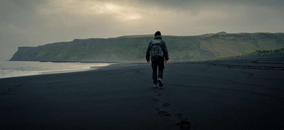 A lone traveler walking on the black sands of Vík í Mýrdal, Iceland's moody landscape.