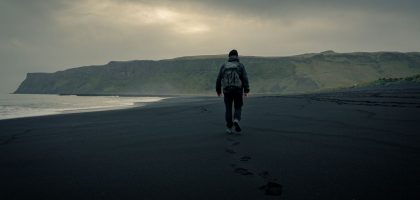 A lone traveler walking on the black sands of Vík í Mýrdal, Iceland's moody landscape.