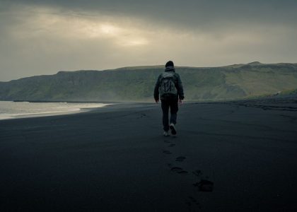 A lone traveler walking on the black sands of Vík í Mýrdal, Iceland's moody landscape.